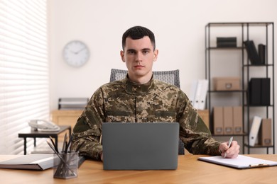 Photo of Military service. Young soldier working at wooden table in office