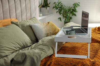 Photo of White tray with modern laptop and cup of aromatic drink on bed indoors, space for text