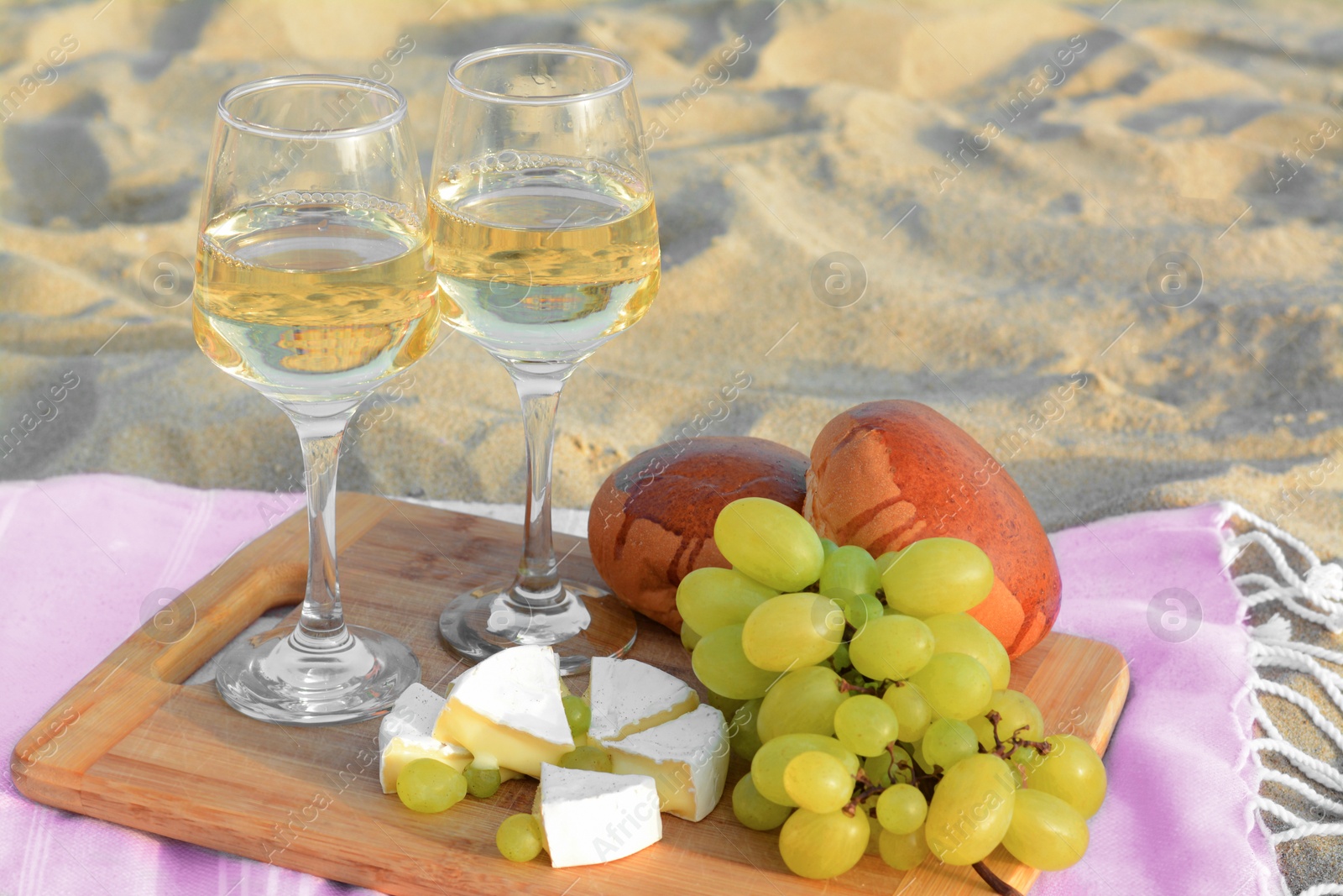 Photo of Glasses with white wine and snacks for beach picnic on sand outdoors