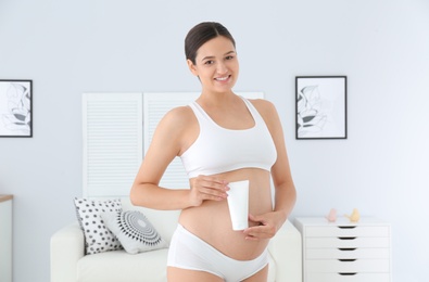 Photo of Pregnant woman holding body cream at home