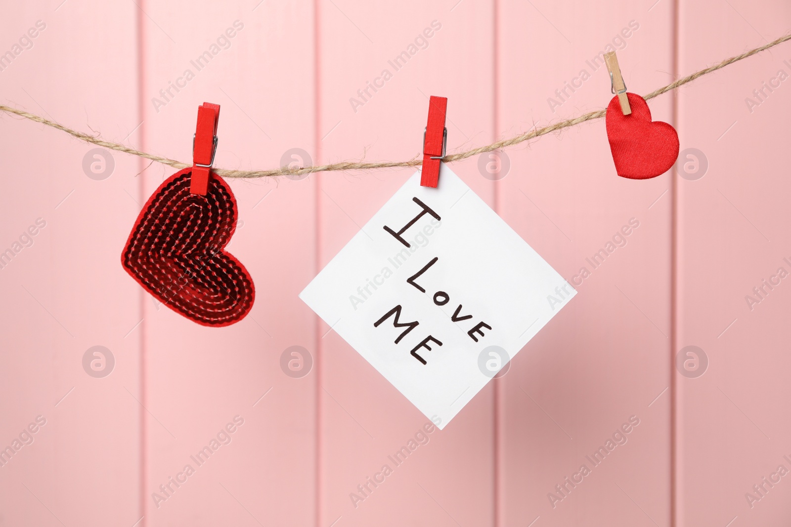 Photo of Hearts and paper note with phrase I Love Me hanging against pink wooden wall