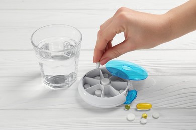 Woman putting pill into plastic box at white wooden table, closeup