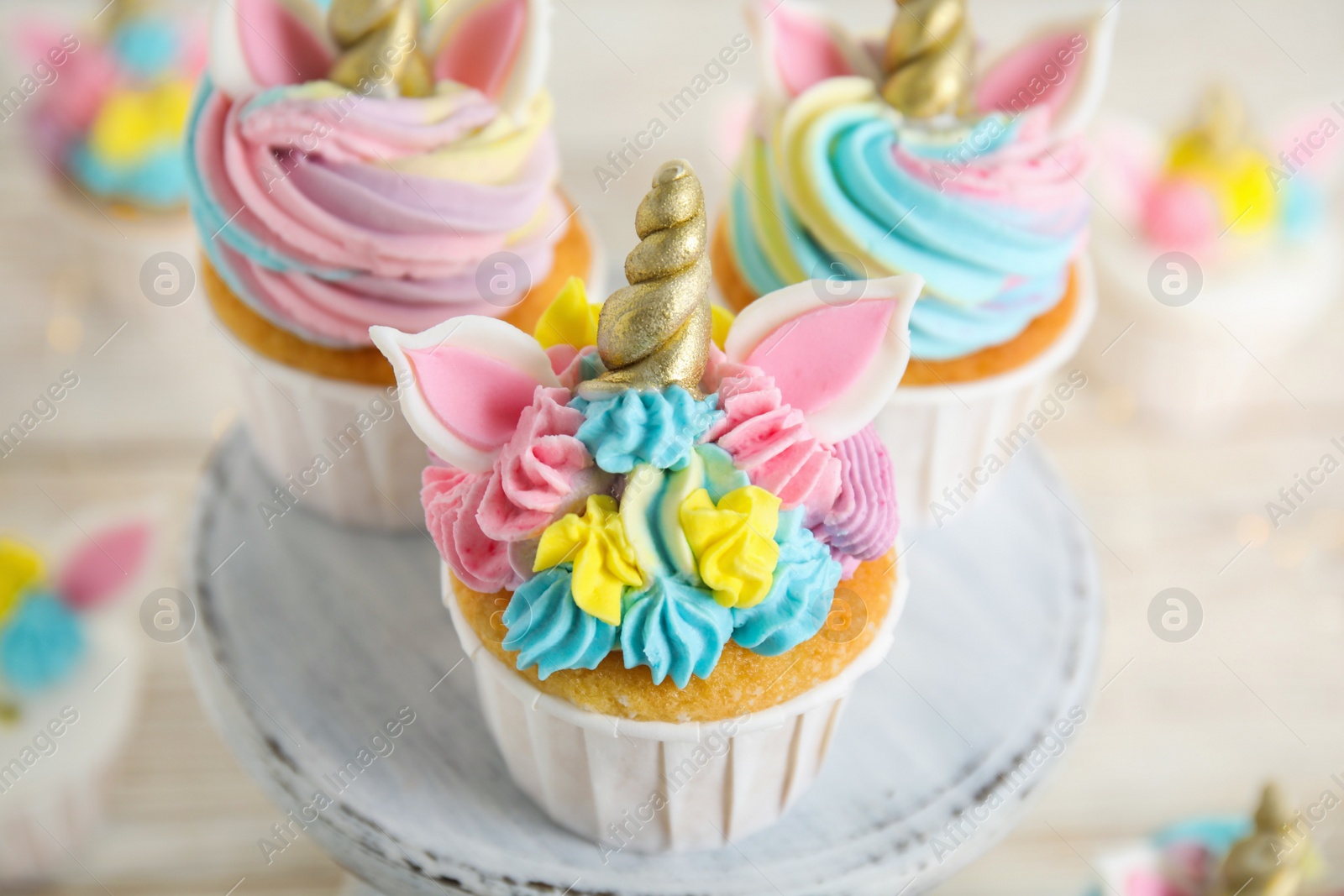 Photo of Dessert stand with cute sweet unicorn cupcakes on white table, closeup