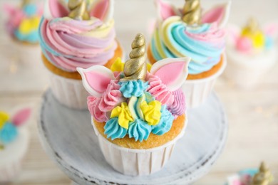 Photo of Dessert stand with cute sweet unicorn cupcakes on white table, closeup