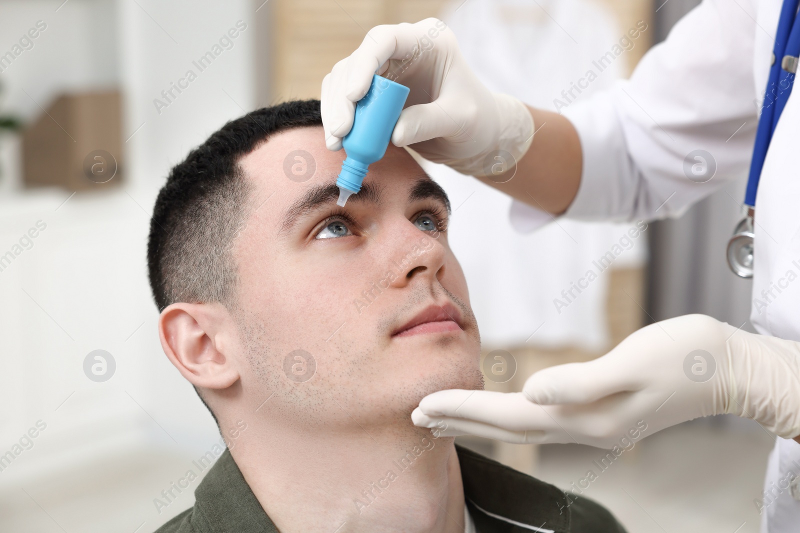 Photo of Doctor applying medical drops into young man's eye indoors