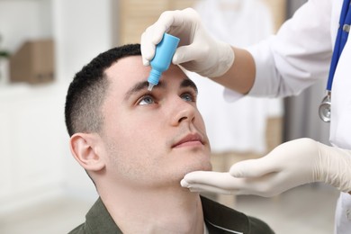 Photo of Doctor applying medical drops into young man's eye indoors