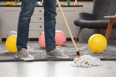 Photo of Man with mop cleaning messy room after party, closeup view of legs