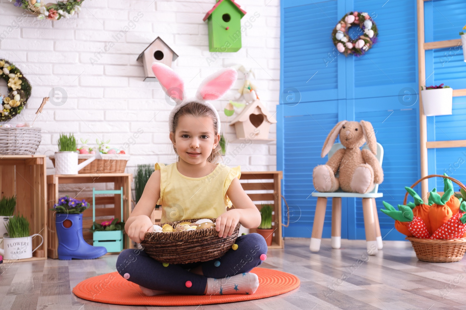 Photo of Adorable little girl with bunny ears and basket full of dyed eggs in Easter photo zone