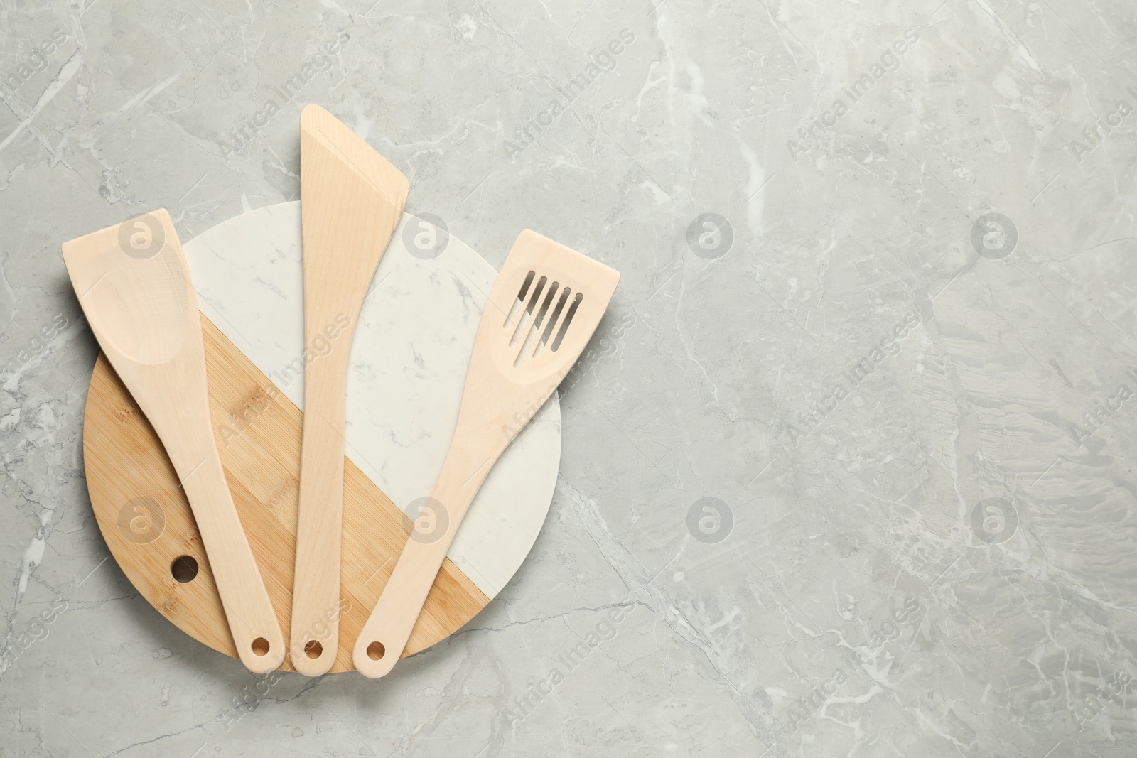 Photo of Different wooden spatulas and board on grey textured table, top view. Space for text