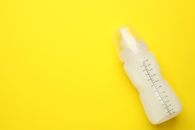 Photo of Feeding bottle with infant formula on yellow background, top view. Space for text