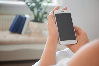 Photo of Young woman holding mobile phone with blank screen in hands indoors
