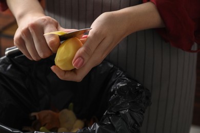 Photo of Woman peeling fresh potato above garbage bin indoors, closeup