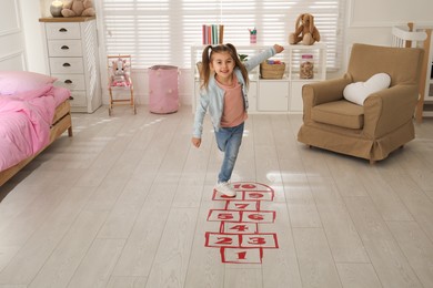 Photo of Cute little girl playing hopscotch at home