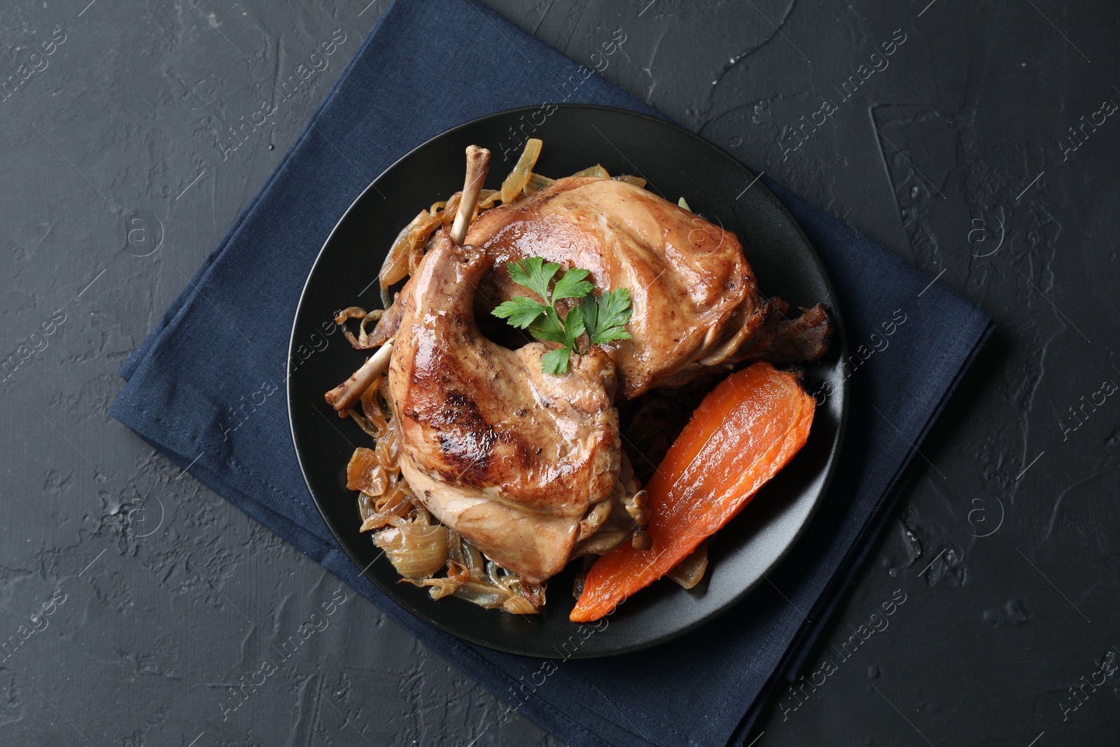 Photo of Tasty cooked rabbit meat with vegetables and parsley on black table, top view