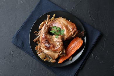 Tasty cooked rabbit meat with vegetables and parsley on black table, top view