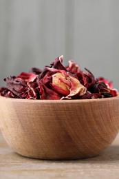 Dry hibiscus tea in bowl on wooden table, closeup. Space for text