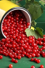 Photo of Many ripe red currants, mug and leaves on green wooden table, closeup