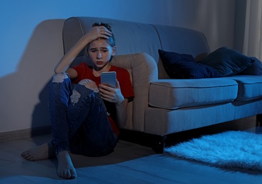 Upset teenage girl with smartphone in dark room. Danger of internet