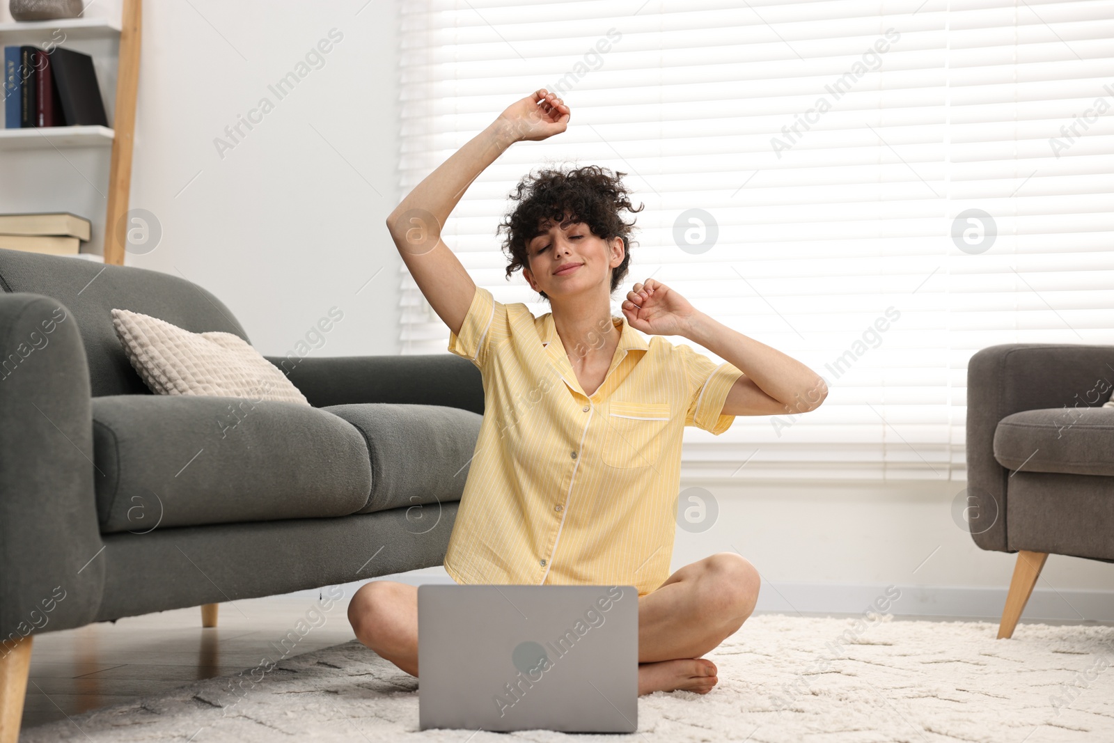 Photo of Beautiful young woman in stylish pyjama with laptop on floor at home