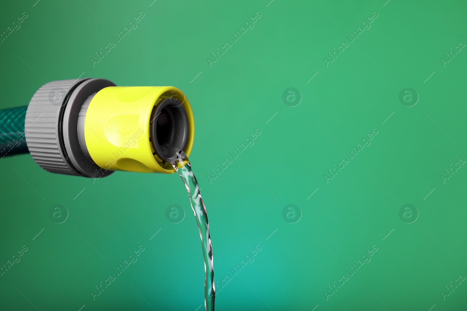 Photo of Water dripping from hose on green background, closeup. Space for text