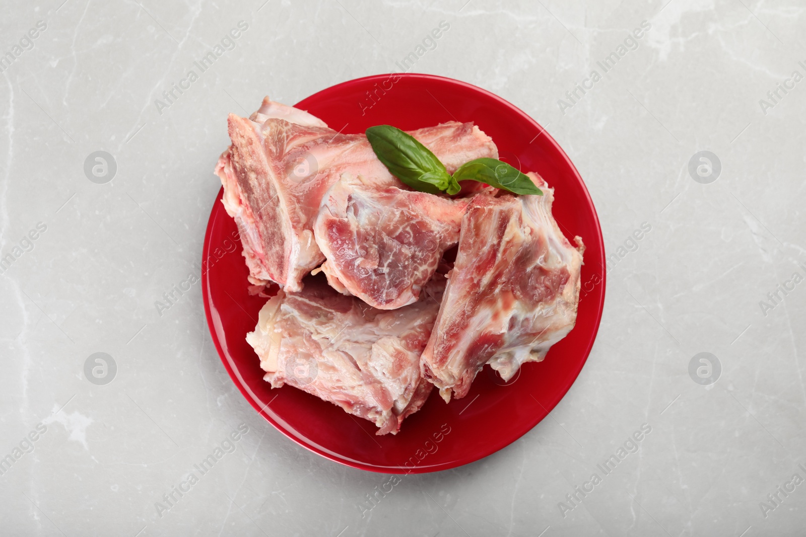 Photo of Plate with raw chopped meaty bones and basil on grey table, top view