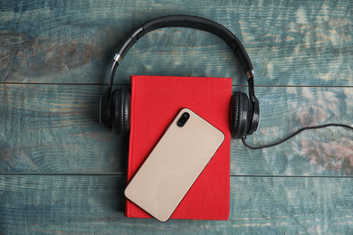 Photo of Book, modern headphones and smartphone on blue wooden table, flat lay