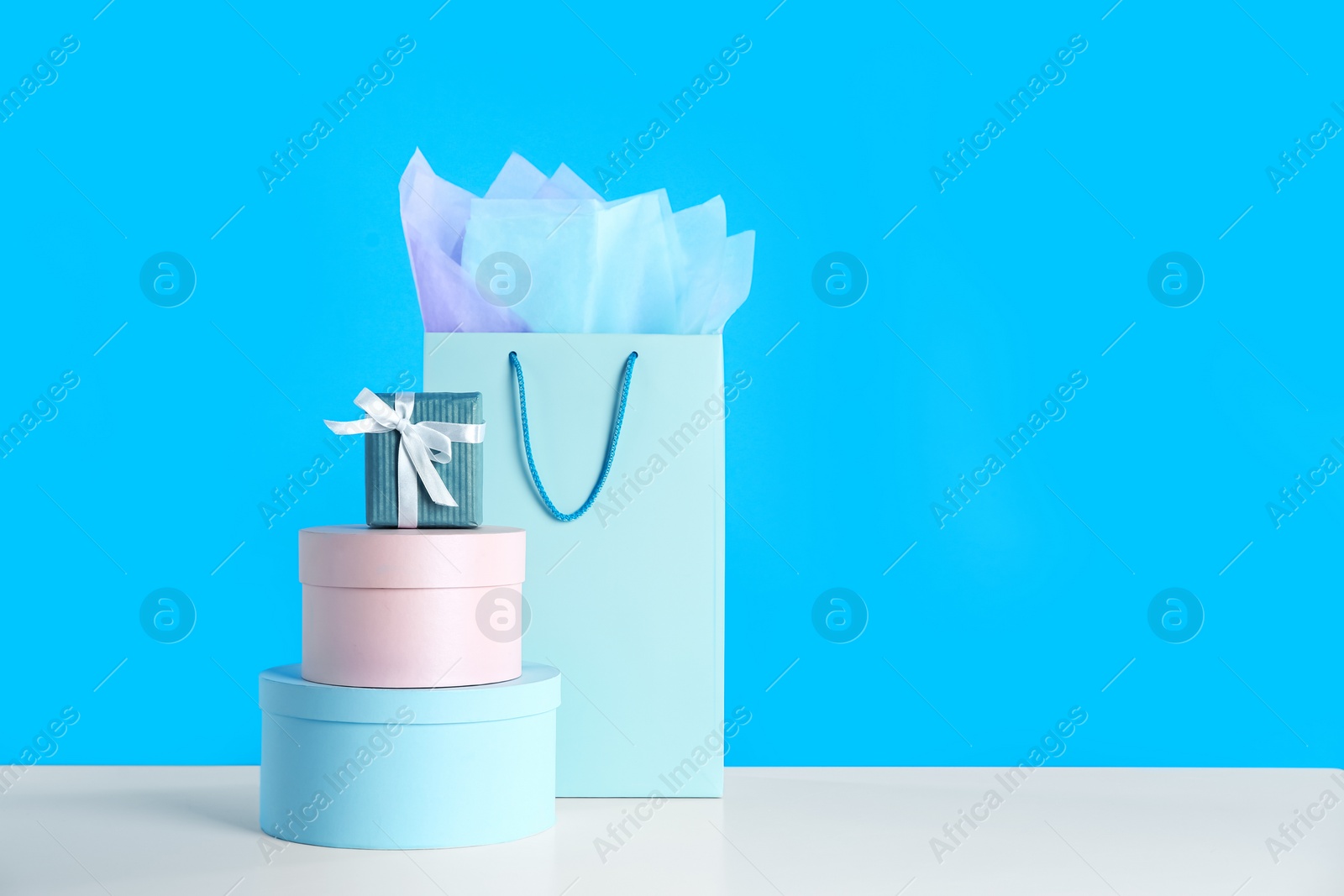 Photo of Gift bag and boxes on white table against light blue background. Space for text