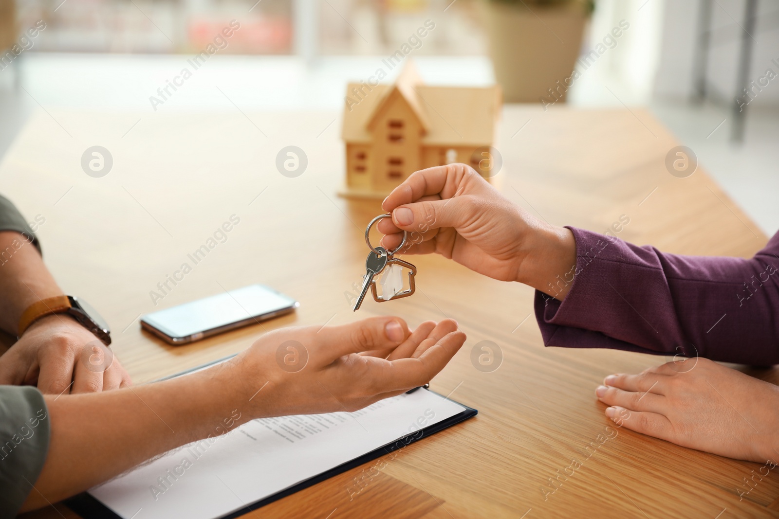 Photo of Real estate agent giving key with trinket to client in office, closeup