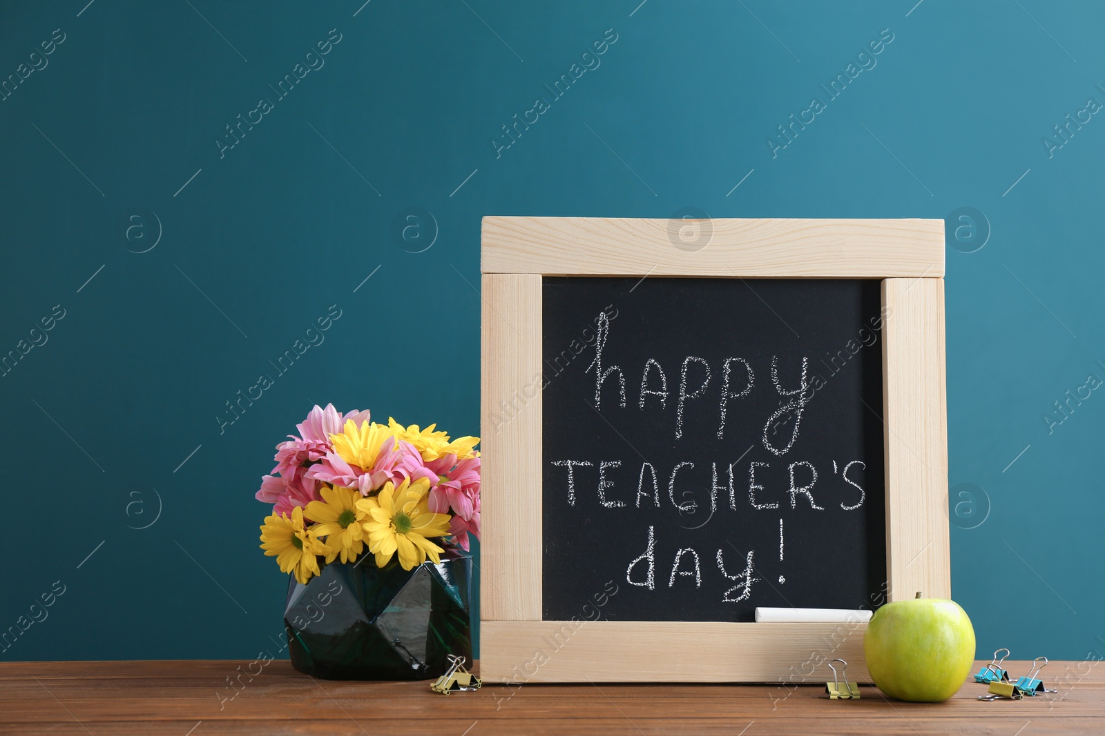 Photo of Little blackboard with inscription HAPPY TEACHER'S DAY, flowers and apple on table