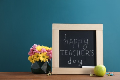 Little blackboard with inscription HAPPY TEACHER'S DAY, flowers and apple on table