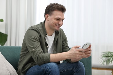 Happy man using smartphone on sofa at home