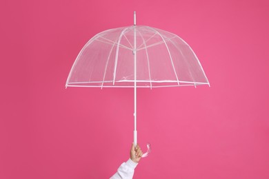 Photo of Woman with open transparent umbrella on pink background, closeup