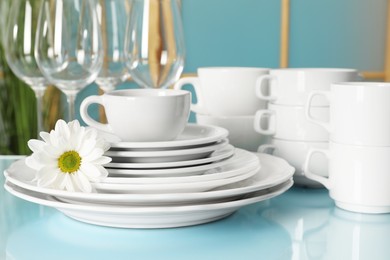 Photo of Set of clean dishware and flower on light blue table, closeup