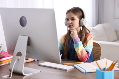 E-learning. Cute girl using computer and headphones during online lesson at table indoors
