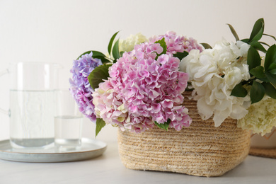 Photo of Beautiful hydrangea flowers in basket on light table, closeup