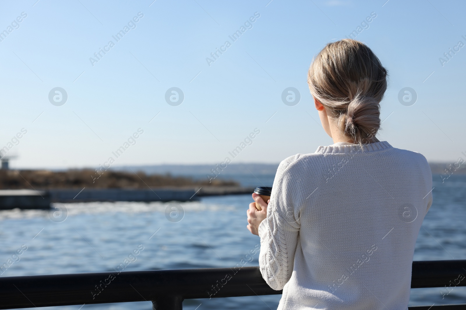 Photo of Lonely woman with cup of drink near river on sunny day, back view