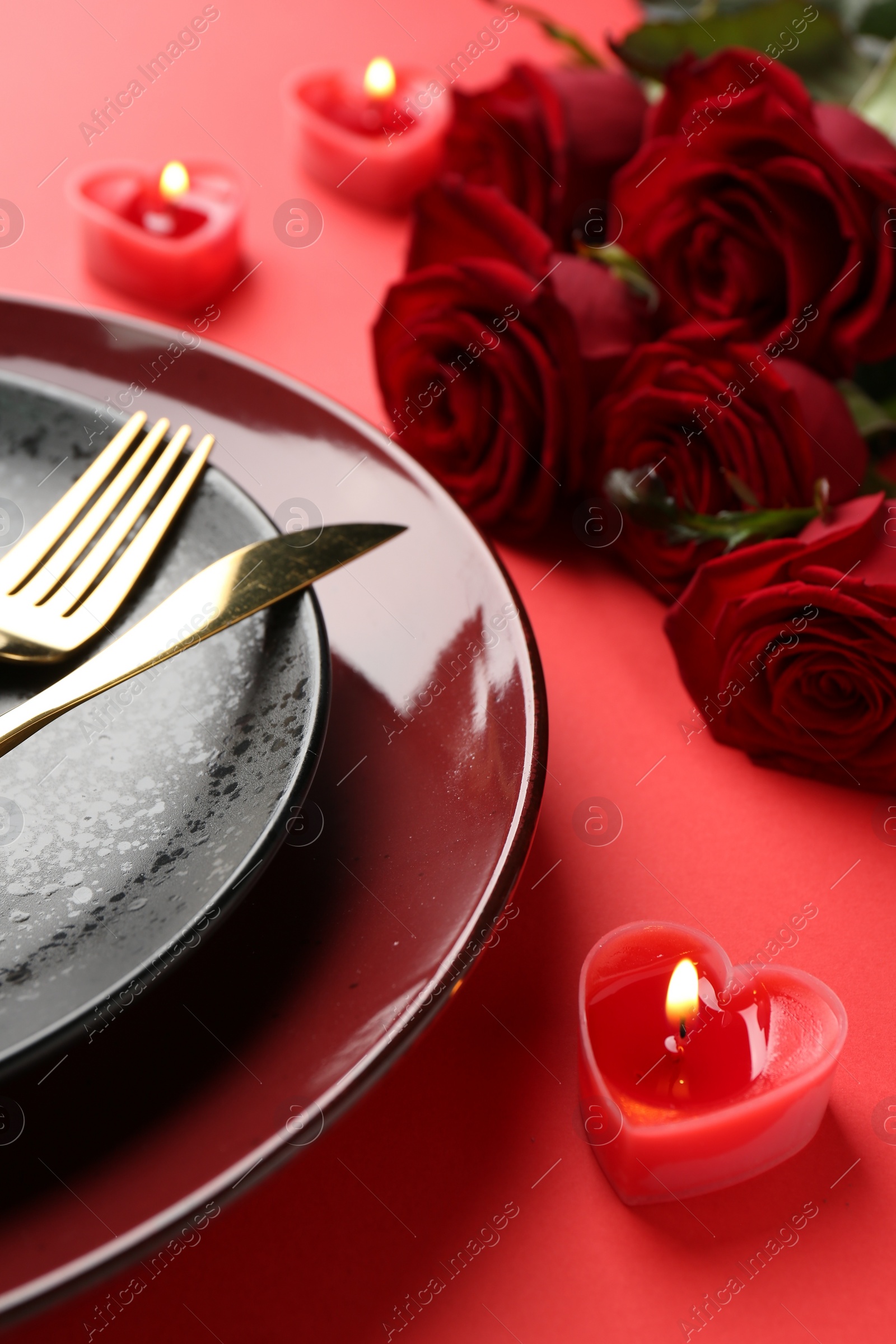 Photo of Place setting with heart shaped candles and bouquet of roses on red table, closeup. Romantic dinner