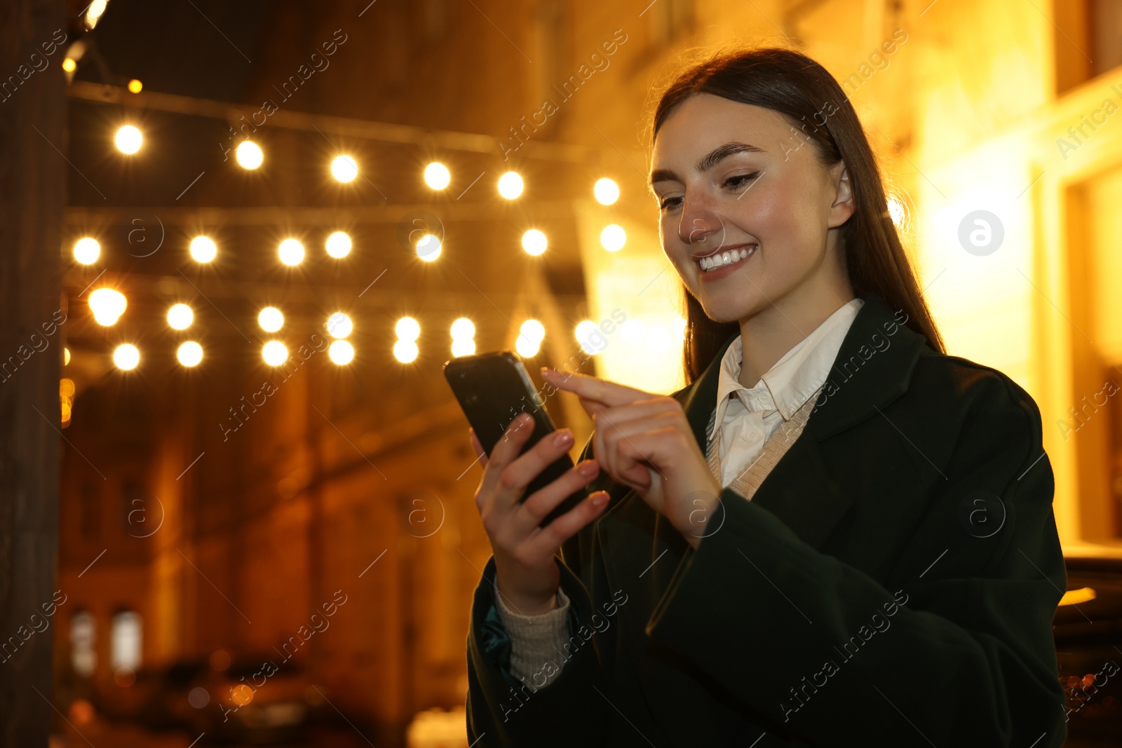 Photo of Smiling woman using smartphone on night city street. Space for text