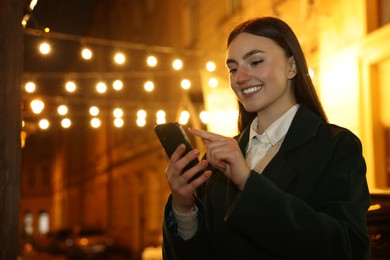Photo of Smiling woman using smartphone on night city street. Space for text