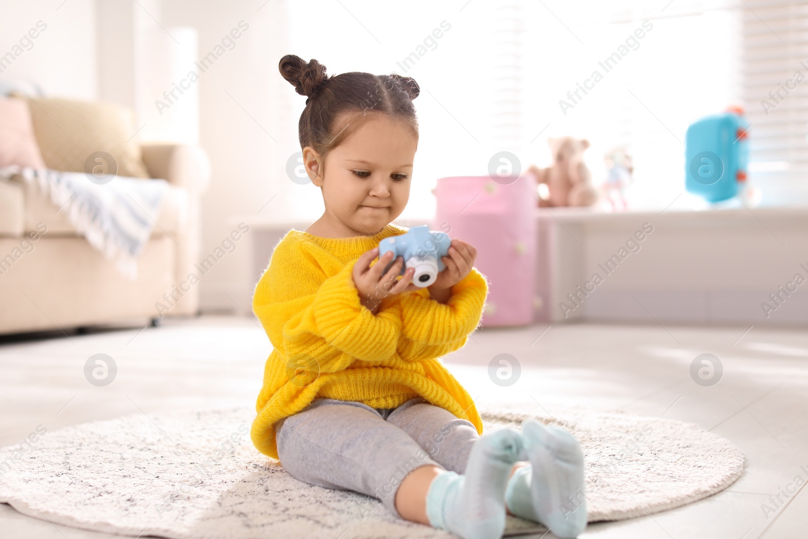 Photo of Little photographer with toy camera on floor at home