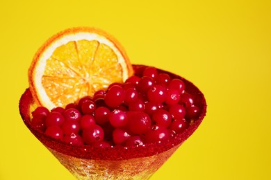 Martini glass with cranberries and dry orange slice on yellow background, closeup
