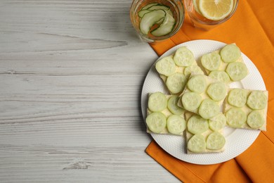 Photo of Tasty sandwiches with butter and cucumber served on white wooden table, flat lay. Space for text