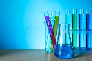 Different laboratory glassware with colorful liquids on wooden table against light blue background. Space for text