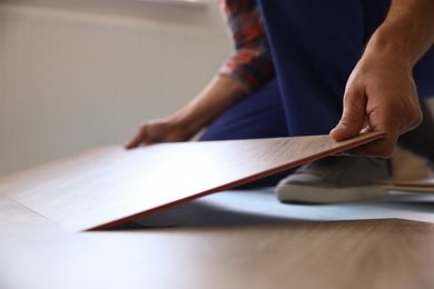 Photo of Worker installing laminated wooden floor indoors, closeup