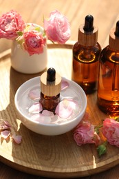 Photo of Bottles of rose essential oil and flowers on wooden table