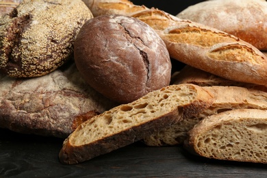 Photo of Different kinds of fresh bread on black wooden table, closeup