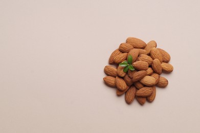 Photo of Delicious almonds and fresh leaves on beige background, top view. Space for text