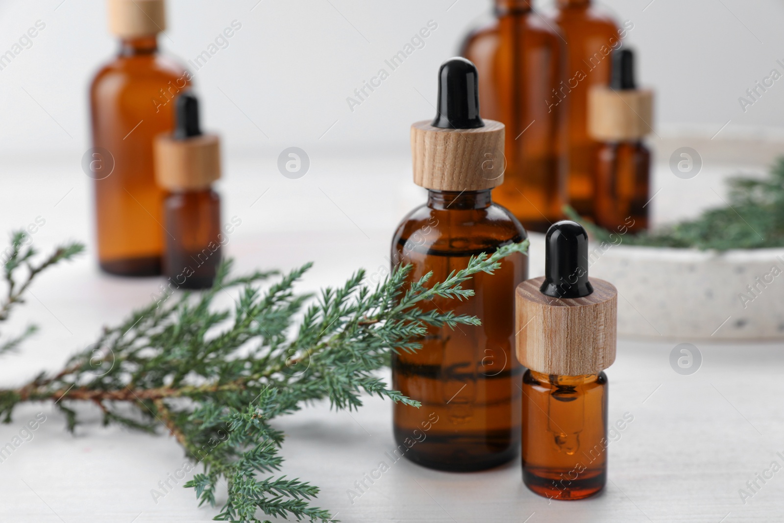 Photo of Bottles of juniper essential oil and fresh twig on white wooden table