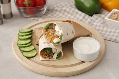 Delicious tortilla wraps with tuna, cucumber slices and sauce on light grey table