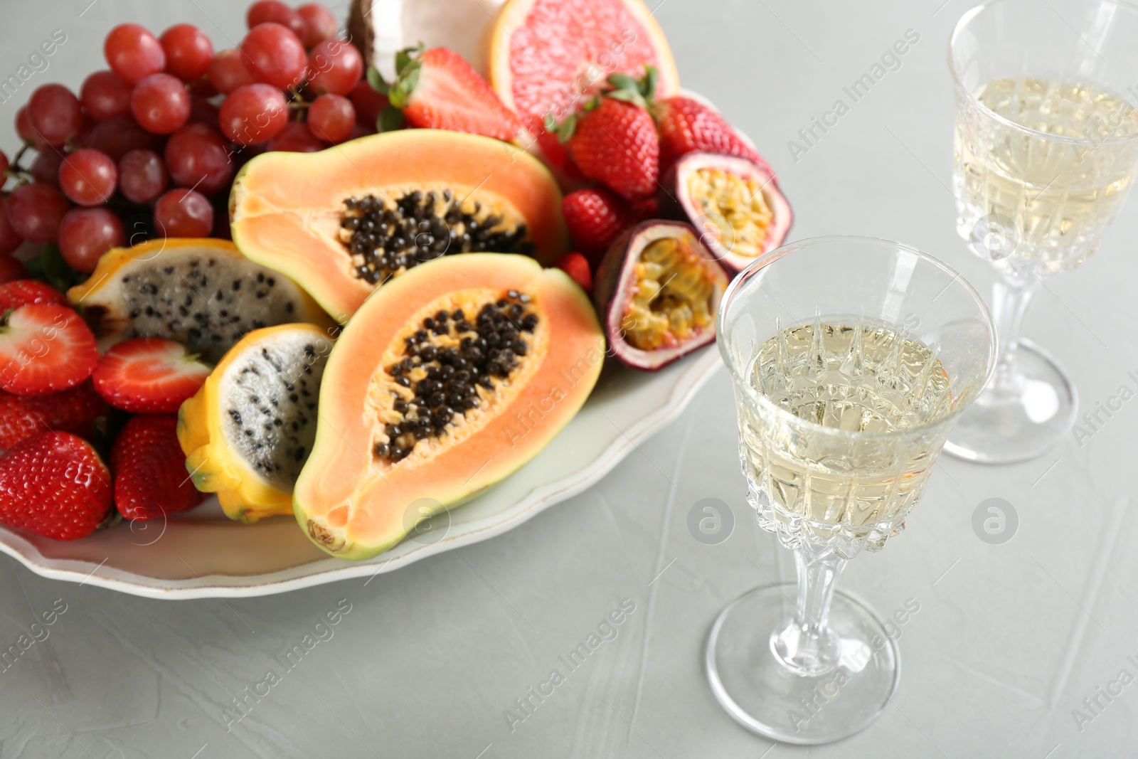 Photo of Delicious exotic fruits and glasses of wine on light grey table